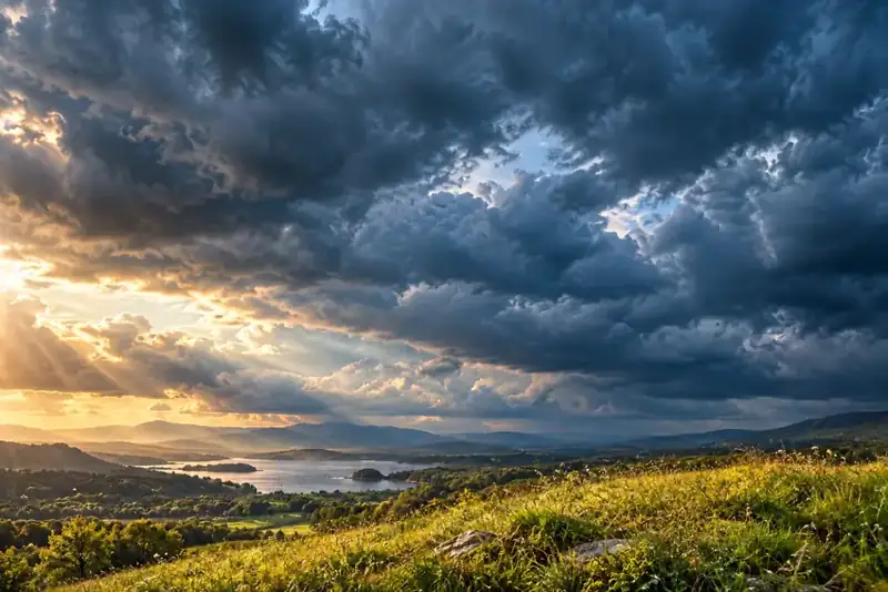Sunlight over a meadow and lake beneath storm clouds